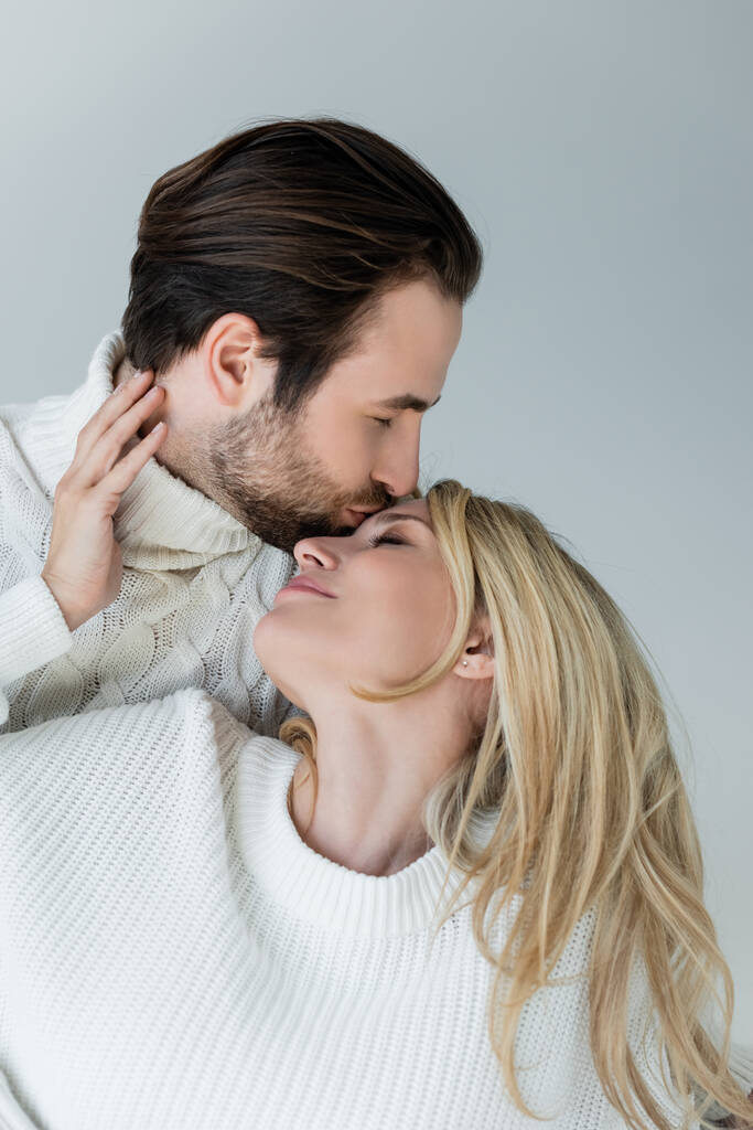 bearded man kissing forehead of blonde girlfriend in sweater isolated on grey - Zdjęcie, obraz