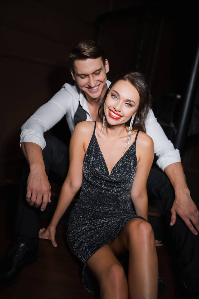Smiling man in shirt looking at elegant girlfriend in dress at home in evening  - Fotografie, Obrázek