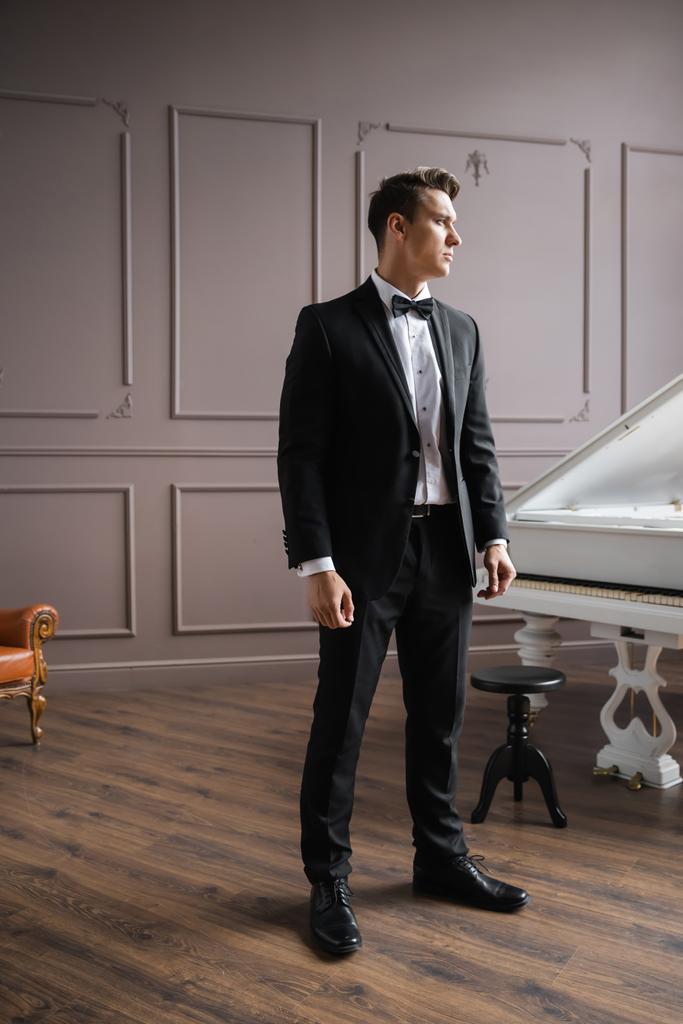 Элегантный мужчина в костюме стоит у фортепиано дома  - Фото, изображение