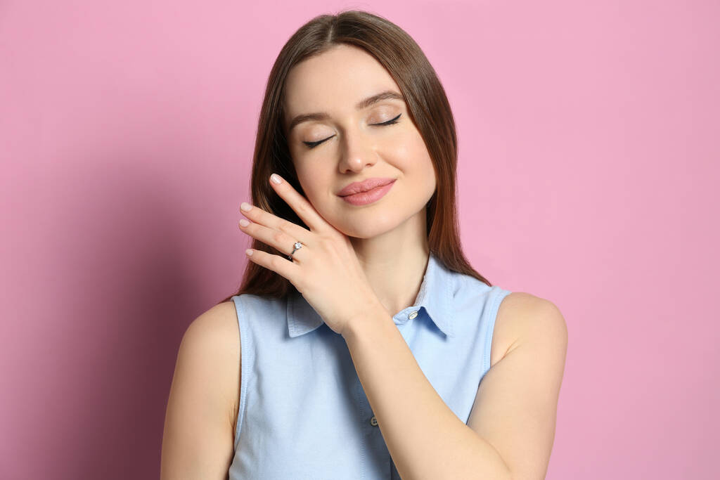 Mujer joven y feliz con hermoso anillo de compromiso sobre fondo rosa - Foto, imagen