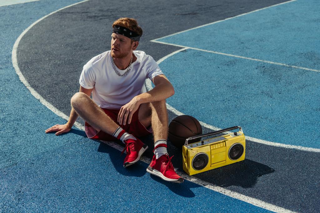 basketball player in red sneakers and bandana sitting on court near boombox - Foto, afbeelding