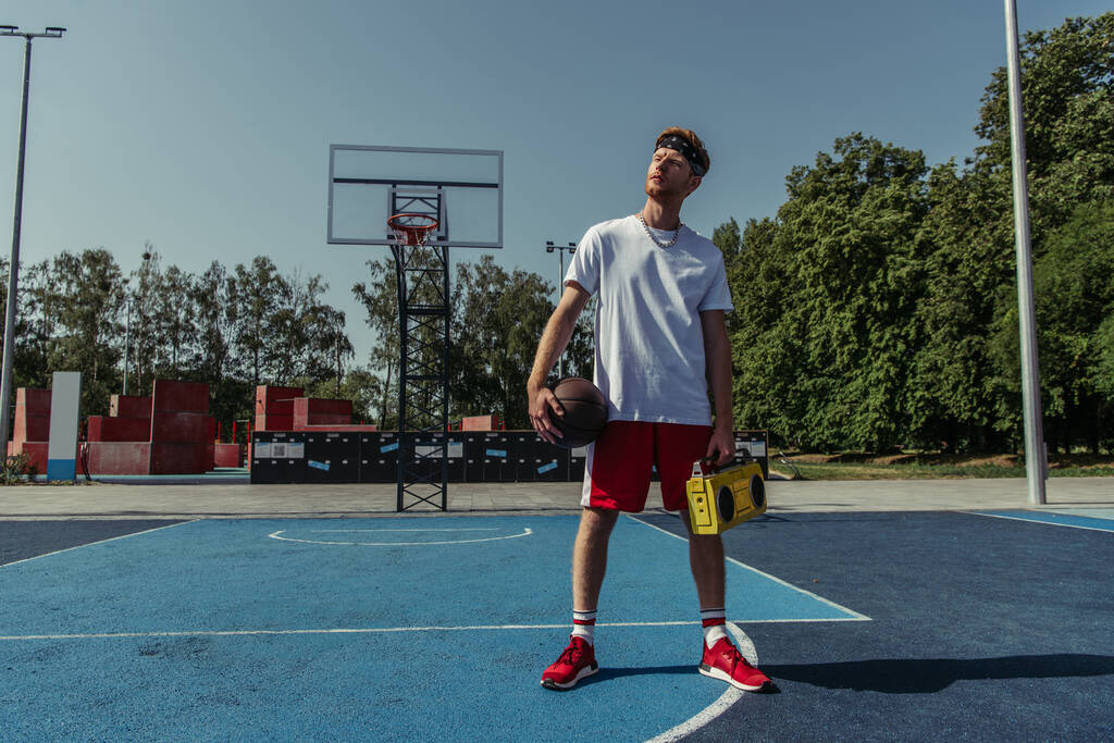полная длина баскетболиста, стоящего на корте с магнитофоном и мячом - Фото, изображение