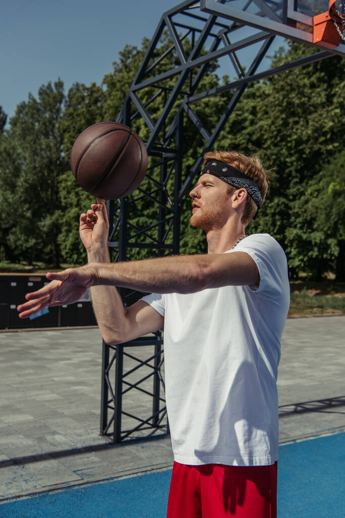 young basketball player in white t-shirt spinning ball on finger outdoors - Foto, Imagem