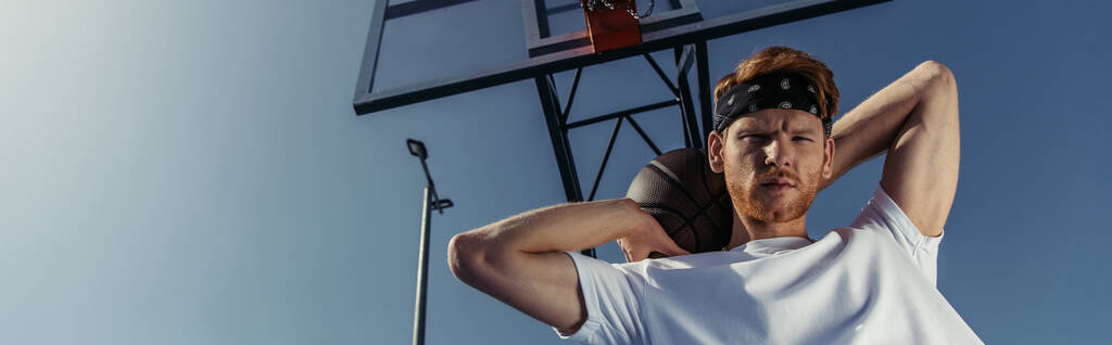 низький кут зору баскетболіста в бандані тримає м'яч і дивиться на камеру, банер
 - Фото, зображення