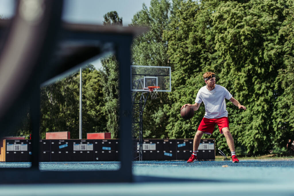 full length of man in sportswear playing basketball outdoors on blurred foreground - Photo, image