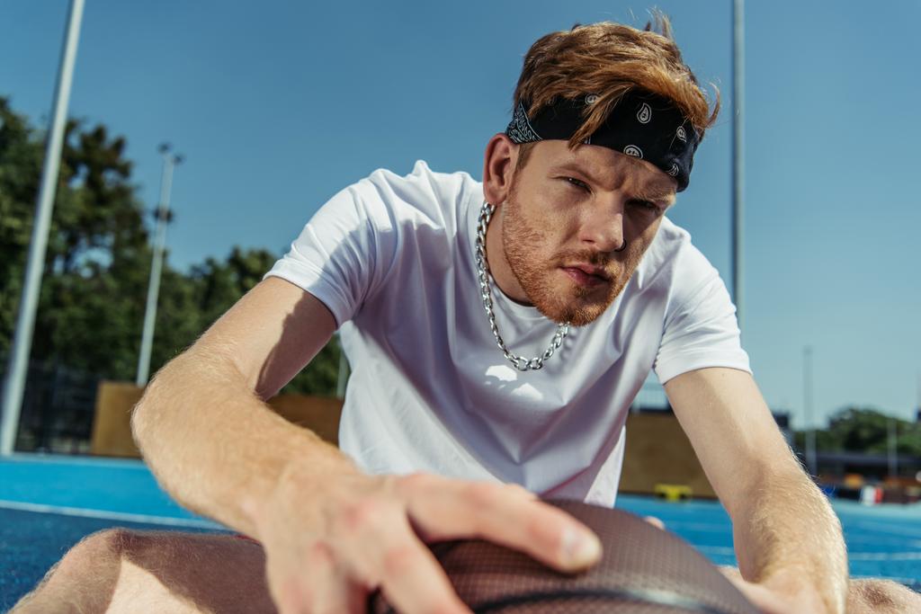 young sportsman in bandana and necklace sitting near blurred ball - Foto, Imagen