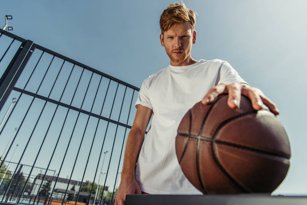 low angle view of confident basketball player looking at camera near blurred ball - Foto, Bild