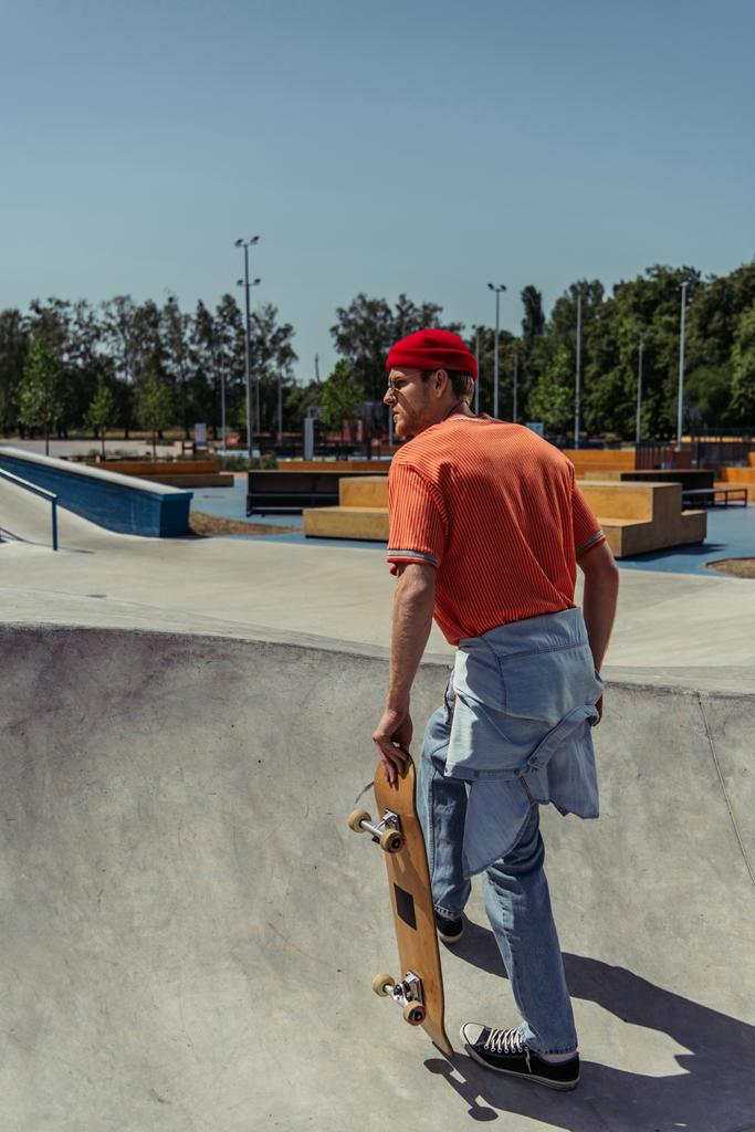 молодой человек в оранжевой футболке и джинсах идет по пандусу со скейтбордом - Фото, изображение