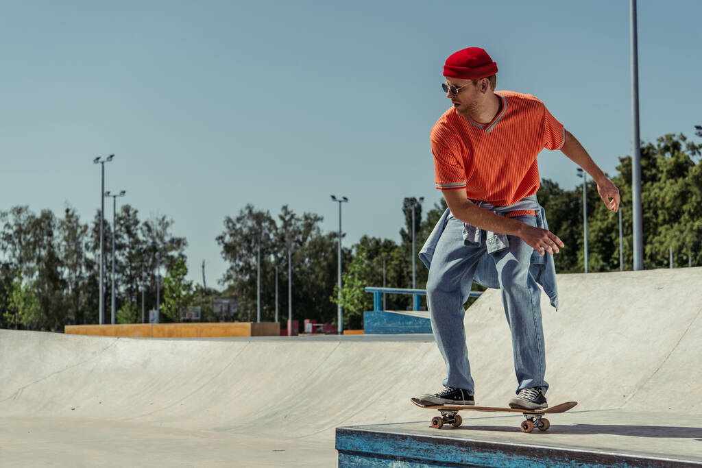 full length of trendy man in jeans riding skateboard on ramp in skate park - 写真・画像