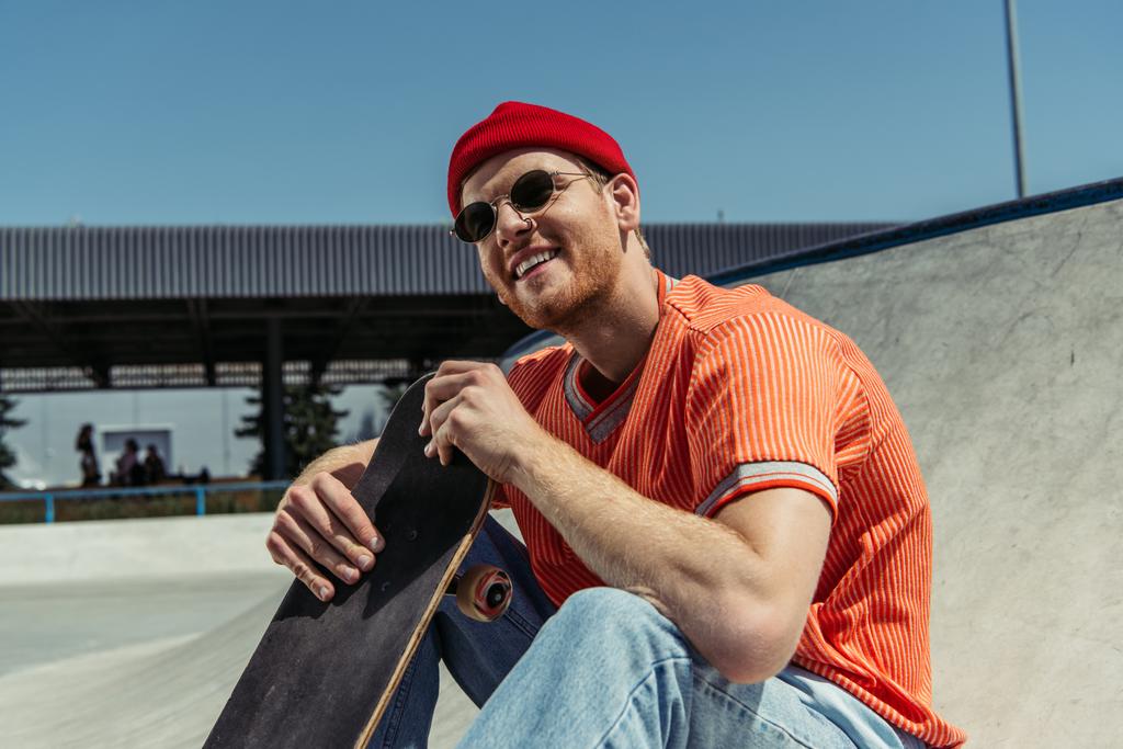 happy man in stylish outfit sitting with skateboard outdoors - Fotoğraf, Görsel