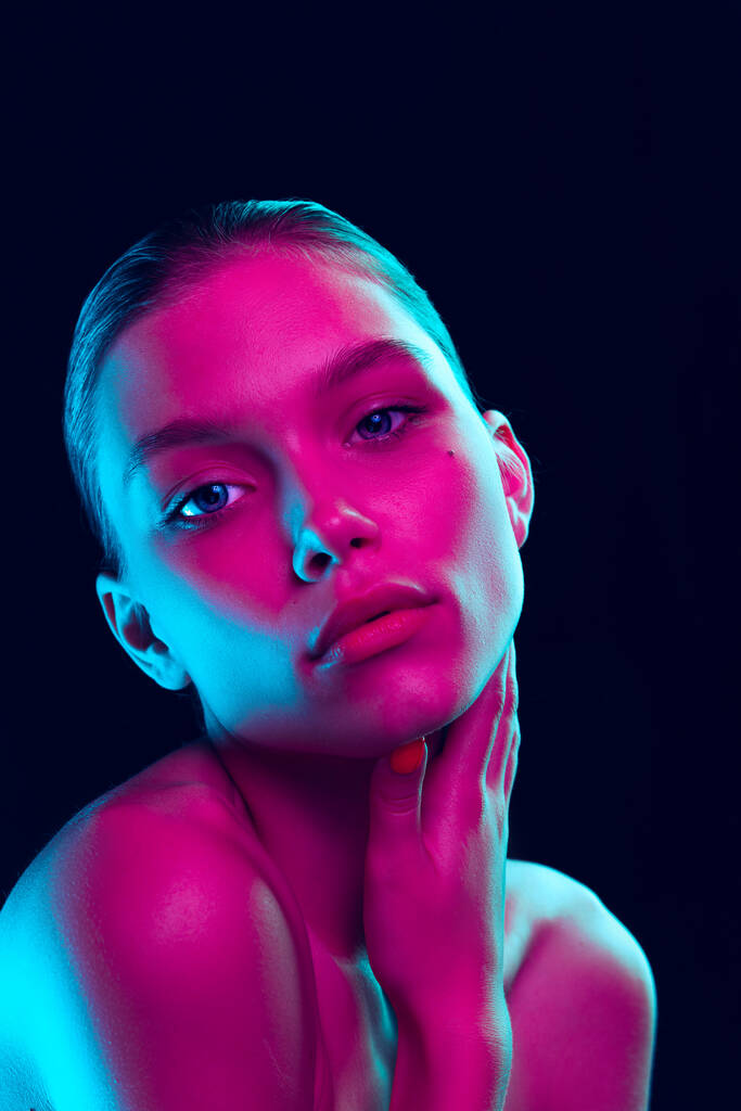 Perfection. Portrait of tender young woman with well-kept skin posing isolated over dark background in neon light. Concept of natural beauty, art, emotions, cosmetics and youth - Zdjęcie, obraz