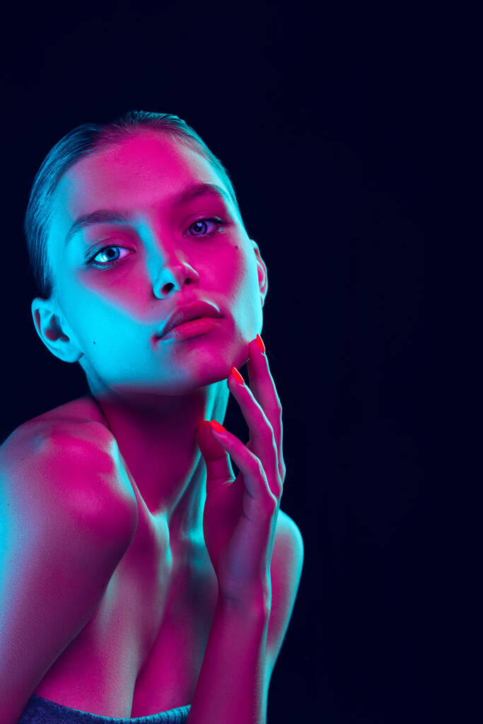 Fashion, style. Young beautiful girl with well-kept skin and without makeup isolated over dark background in neon light. Concept of natural beauty, art, emotions, cosmetics and youth - Foto, immagini