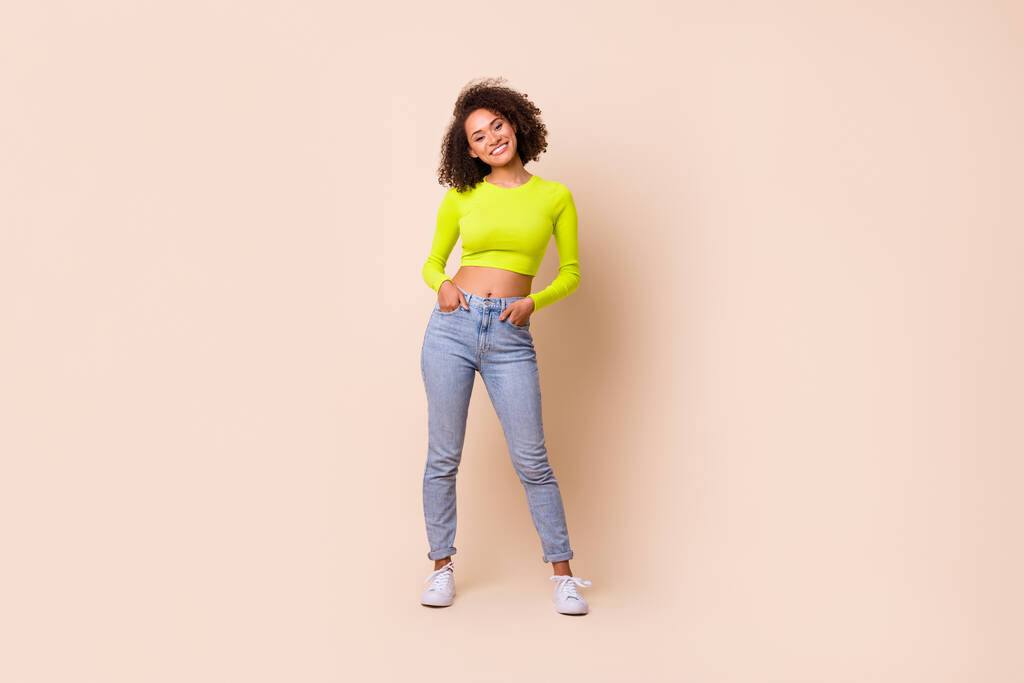 Full body photo of charming young lady curly hair smile hold arms pockets dressed stylish yellow clothes isolated on beige color background. - Fotó, kép