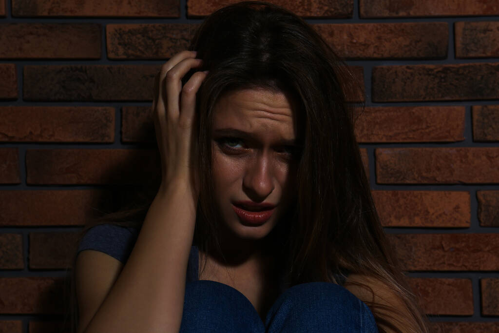 Κακοποιημένη νεαρή γυναίκα που κλαίει κοντά σε τοίχο από τούβλα. Έννοια της ενδοοικογενειακής βίας - Φωτογραφία, εικόνα