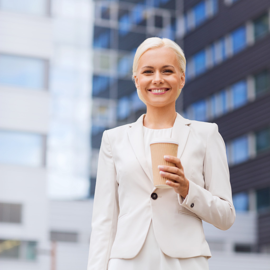 Glimlachende zakenvrouw met papier kop buitenshuis - Foto, afbeelding