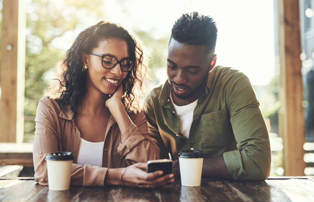 Ένας άλλος τρόπος που η τεχνολογία συνδέει τους ανθρώπους. ένα νεαρό ζευγάρι που χρησιμοποιεί ένα κινητό τηλέφωνο μαζί σε ένα καφέ - Φωτογραφία, εικόνα