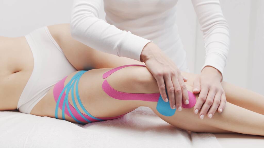 Therapist is applying tape to beautiful female body. Physiotherapy, kinesiology and recovery treatment. - Foto, Imagen