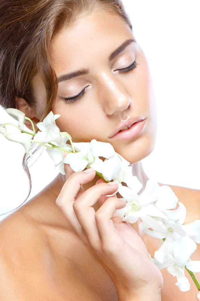 Jeune femme au visage clair naturel maquiller ses cheveux avec une fleur blanche sur un fond clair
 - Photo, image