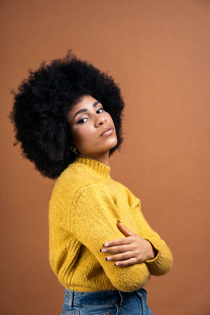 Beautiful young afro woman posing in studio shot against brown background and looking at camera. - Fotoğraf, Görsel