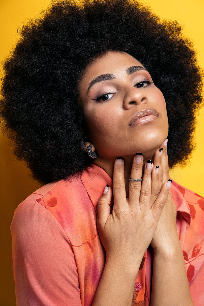 Confident afro woman posing in studio shot and looking at camera against yellow background. - Fotó, kép