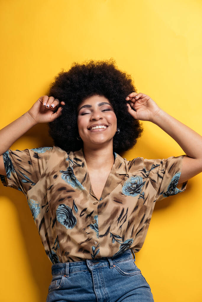 Smiley afro woman wearing colorful shirt having fun in studio shot against yellow background. - Foto, imagen