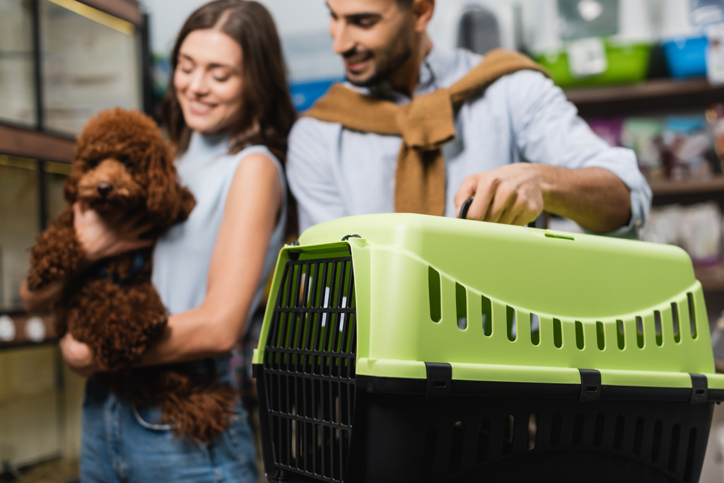 Blurred multiethnic couple with poodle holding animal cage in shop  - Photo, image