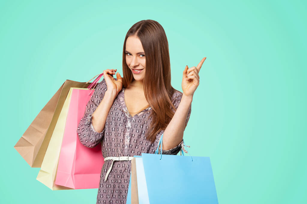 Happy beautiful woman with shopping bags pointing on copy space isolated on green background. - Fotó, kép