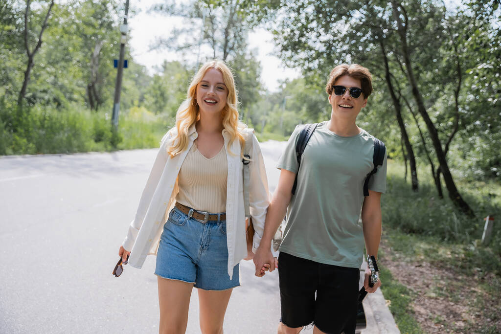 blonde woman and man in sunglasses holding hands while walking in countryside - Foto, Bild