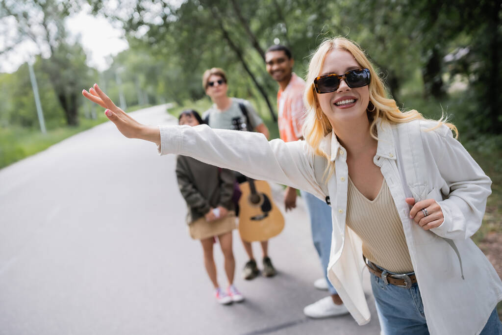 blonde woman in sunglasses stopping car near blurred interracial hitchhikers - Photo, Image