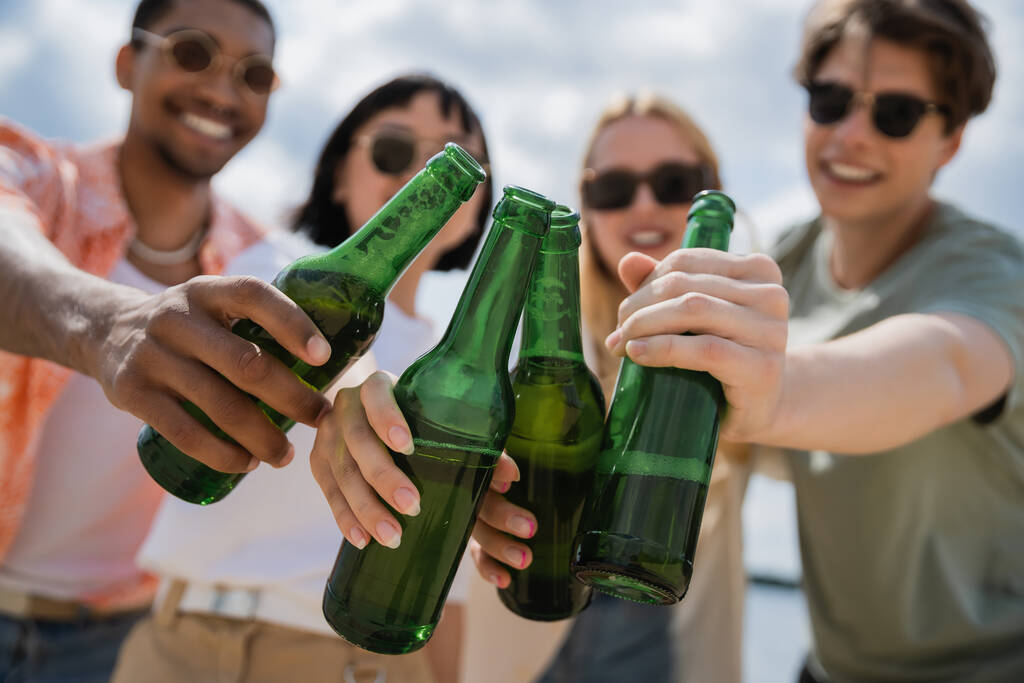 blurred multicultural friends clinking bottles with fresh beer outdoors - Foto, immagini