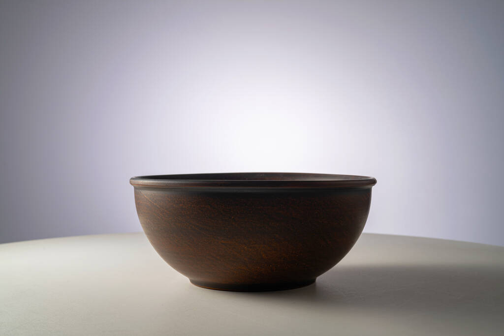 Empty earthen deep bowl on white table isolated on gray studio background. Brown handicraft ramekin or rustic plate. Empty earthenware, crockery from clay for food. Old dishes round shape - 写真・画像