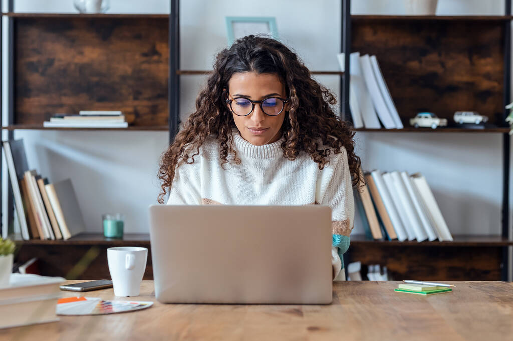 Снимок сконцентрированной красивой деловой женщины, работающей с ноутбуком, когда она пьет кофе в гостиной дома. - Фото, изображение