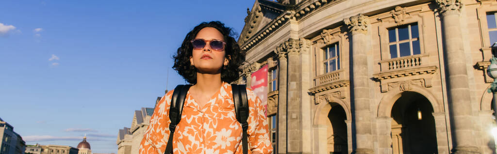 stylish young woman in sunglasses standing near building on museum island, banner - Photo, image