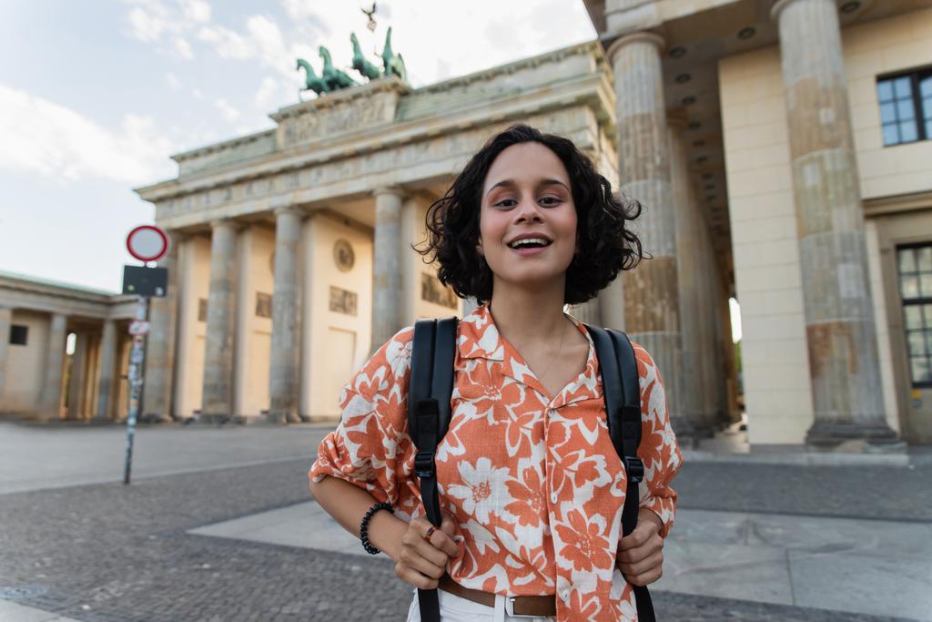 cheerful tourist with backpack standing near brandenburg gate in berlin  - Zdjęcie, obraz