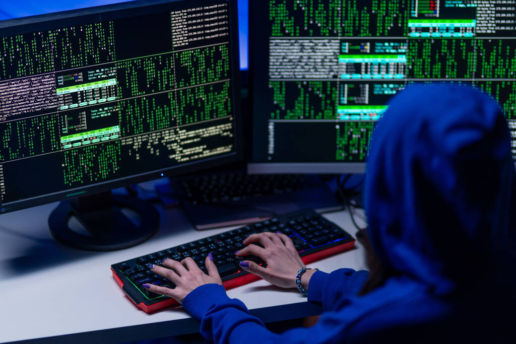 Задний вид на хакера с капюшоном с помощью компьютера в темной комнате ночью, концепция кибервойны. - Фото, изображение