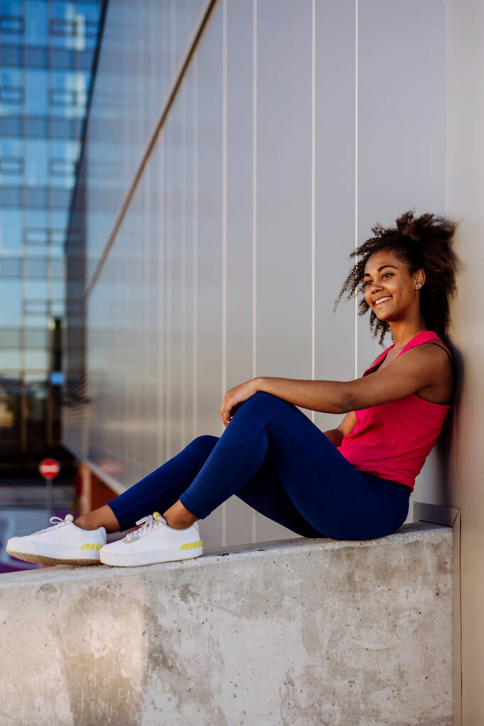 Young multiracial girl in sportswear resting and sitting after jogging in a city. - Photo, Image