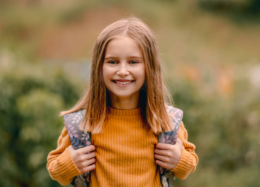 Csinos iskolás lány hátizsákkal, kamerába néz és mosolyog. Gondtalan gyerek ősszel a szabadban portré - Fotó, kép