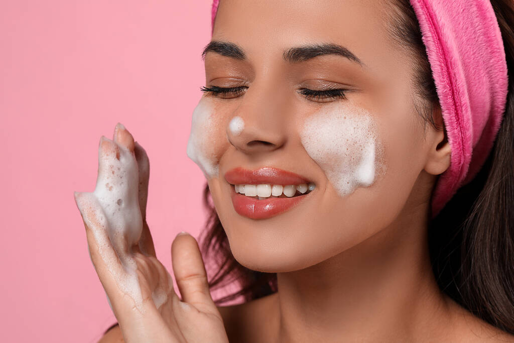 Beautiful woman applying facial cleansing foam on pink background, closeup - Fotó, kép