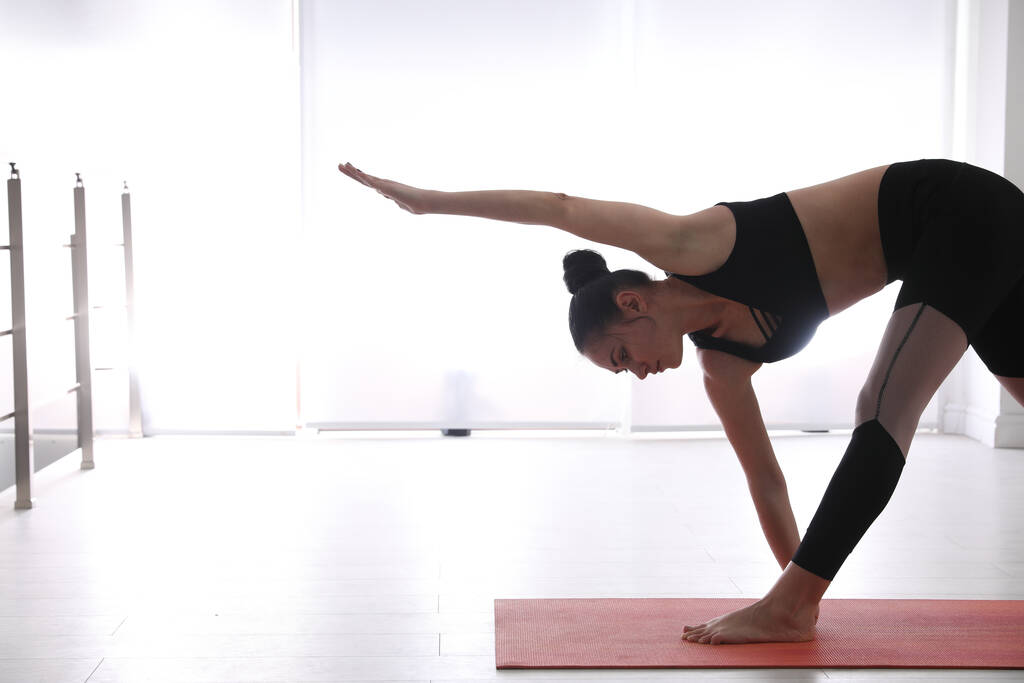 Mladá žena cvičí prodloužený trojúhelník asana v jóga studiu. Utthita Trikonasana pózuje - Fotografie, Obrázek