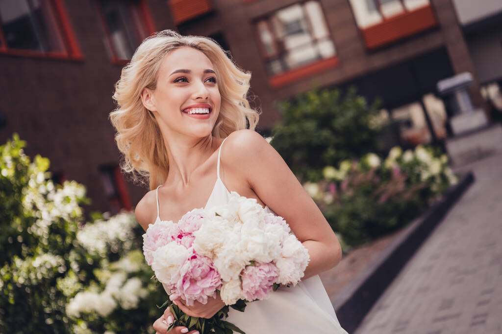 Φωτογραφία από θετική αξιολάτρευτο κυρία απολαμβάνουν ρομαντική ημερομηνία με το φίλο έξω από το σπίτι κατέχουν ανθισμένα μπουκέτο λουλουδιών. - Φωτογραφία, εικόνα