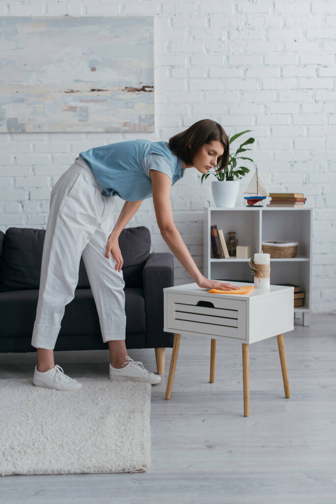 side view of young woman wiping bedside table in living room - Photo, Image