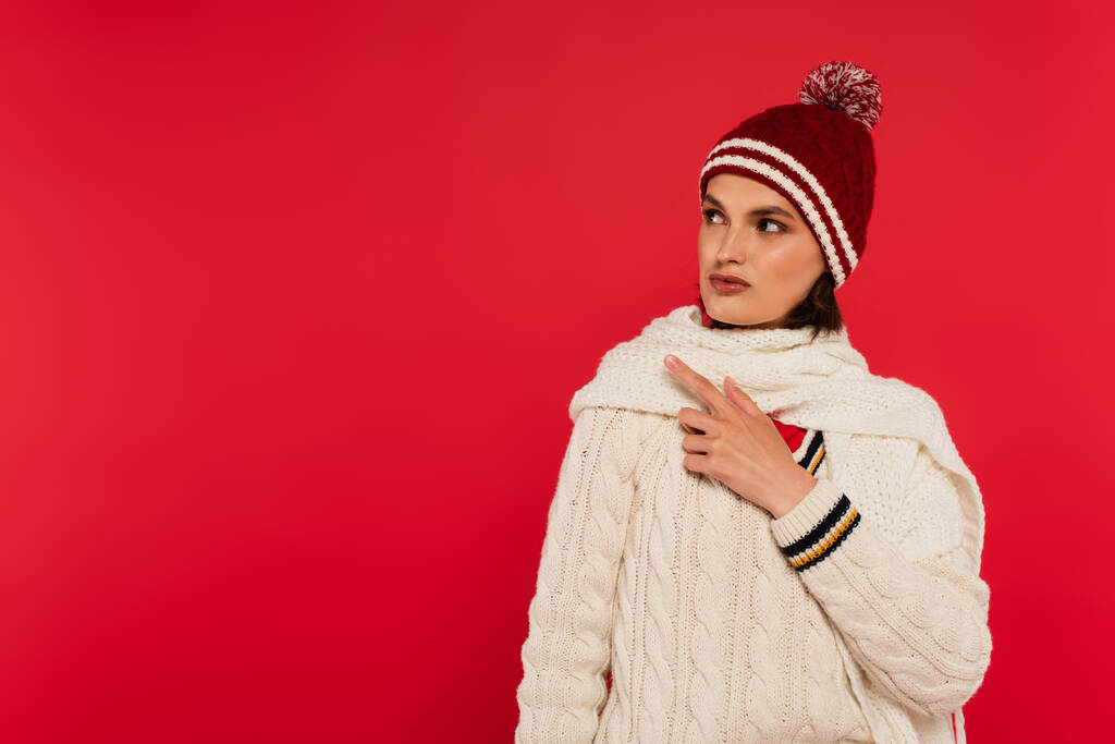 Brunette woman in knitted clothes pointing with finger isolated on red  - Foto, Imagem
