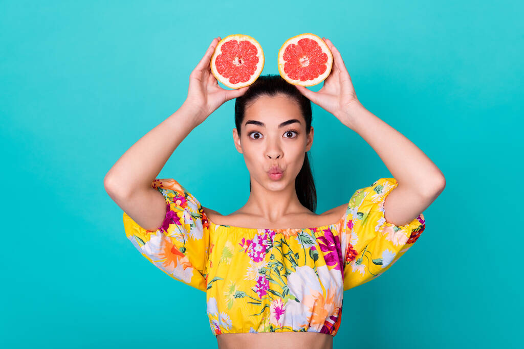 Closeup photo of young cute funny chinese lady joke grimace lips holding grapefruit halves ears isolated on cyan color background. - Fotó, kép