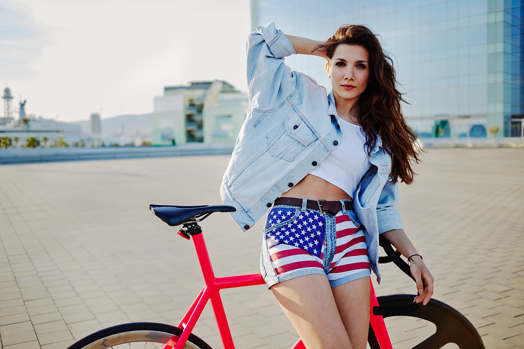 Brązowe włosy kobieta pozowanie z mocowanych na rowerze na świeżym powietrzu, moda dziewczynę stojącą z jej rower patrząc na kamery - Zdjęcie, obraz