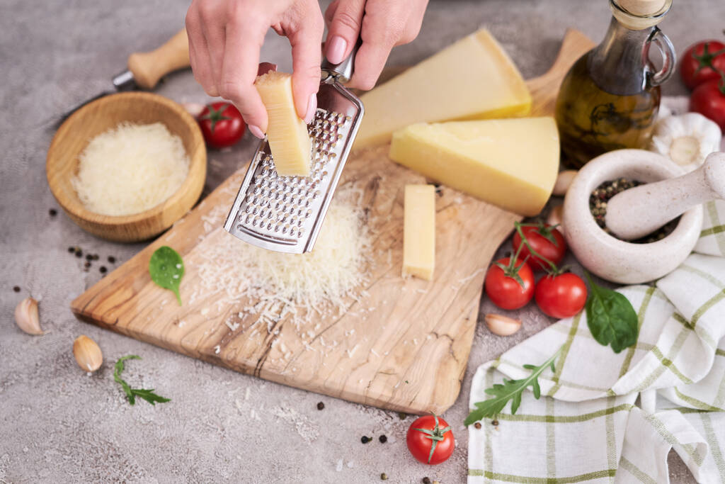Woman grates Parmesan cheese on a wooden cutting board at domestic kitchen. - Zdjęcie, obraz