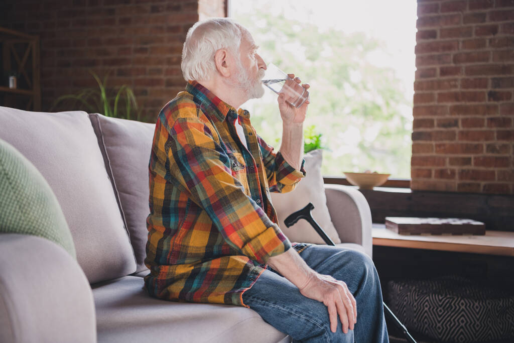 Photo of good mood man pensioner wear checkered shirt drinking fresh water glass indoors house room. - Foto, afbeelding