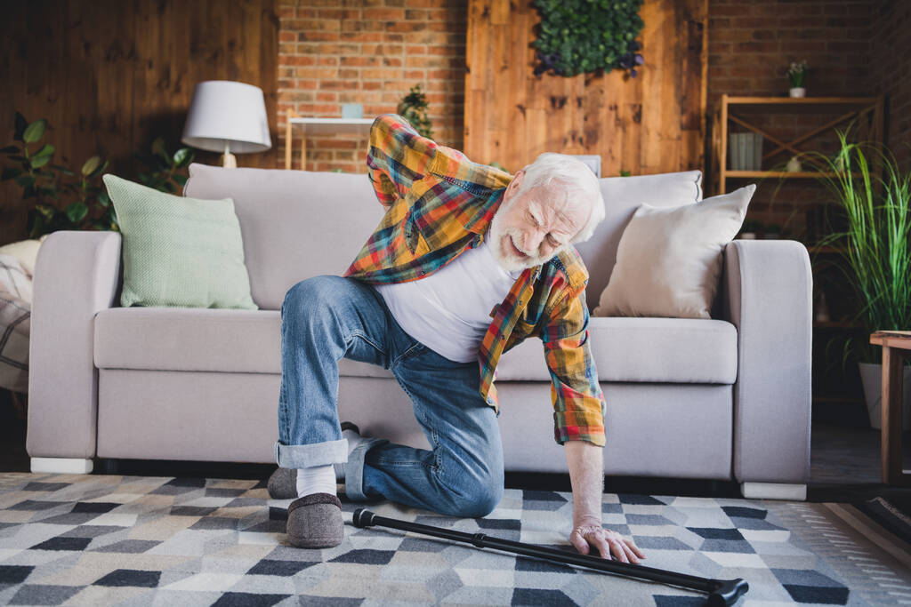 Photo of unhappy upset man pensioner wear checkered shirt falling floor sofa back ache indoors house room. - Fotoğraf, Görsel