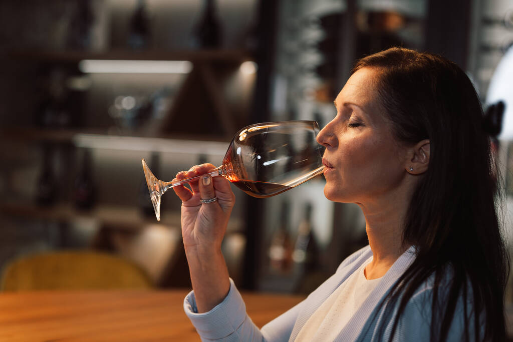 Жінка дегустує вино у винному підвалі з бочками на фоні
 - Фото, зображення