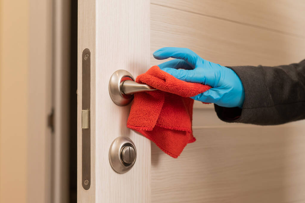 Mujer caucásica con guantes limpia la manija de la puerta con una servilleta - Foto, imagen