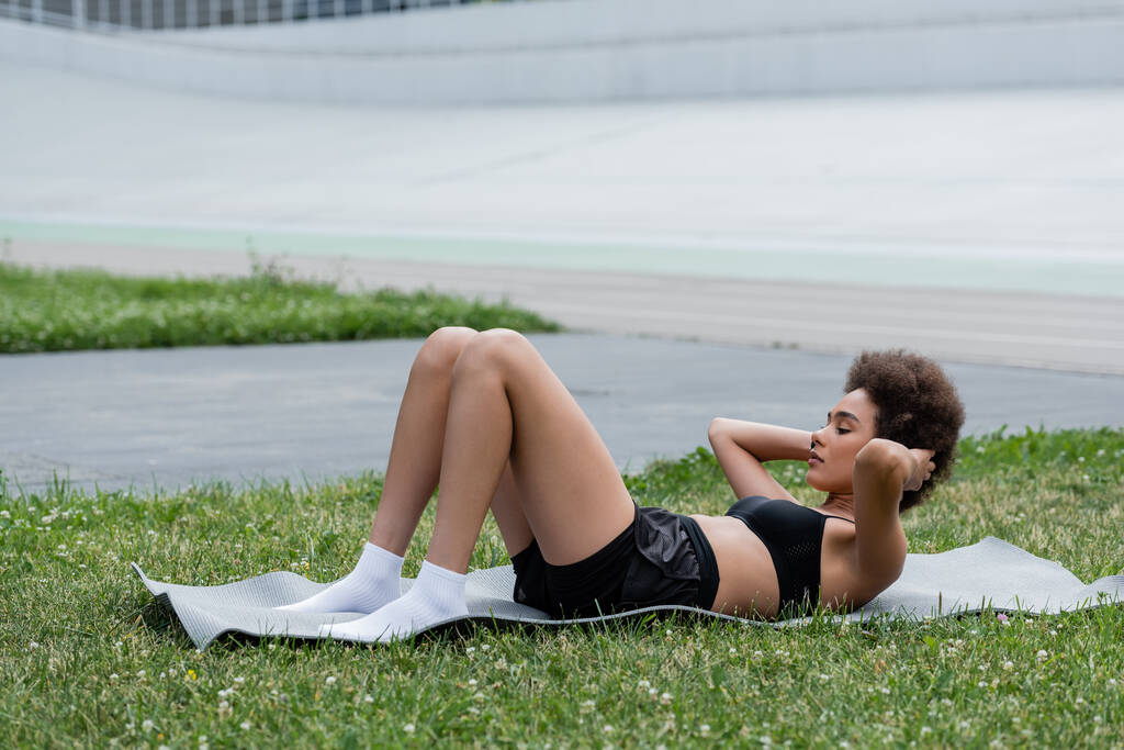 Африканская американская спортсменка тренируется на фитнес-коврике на стадионе  - Фото, изображение